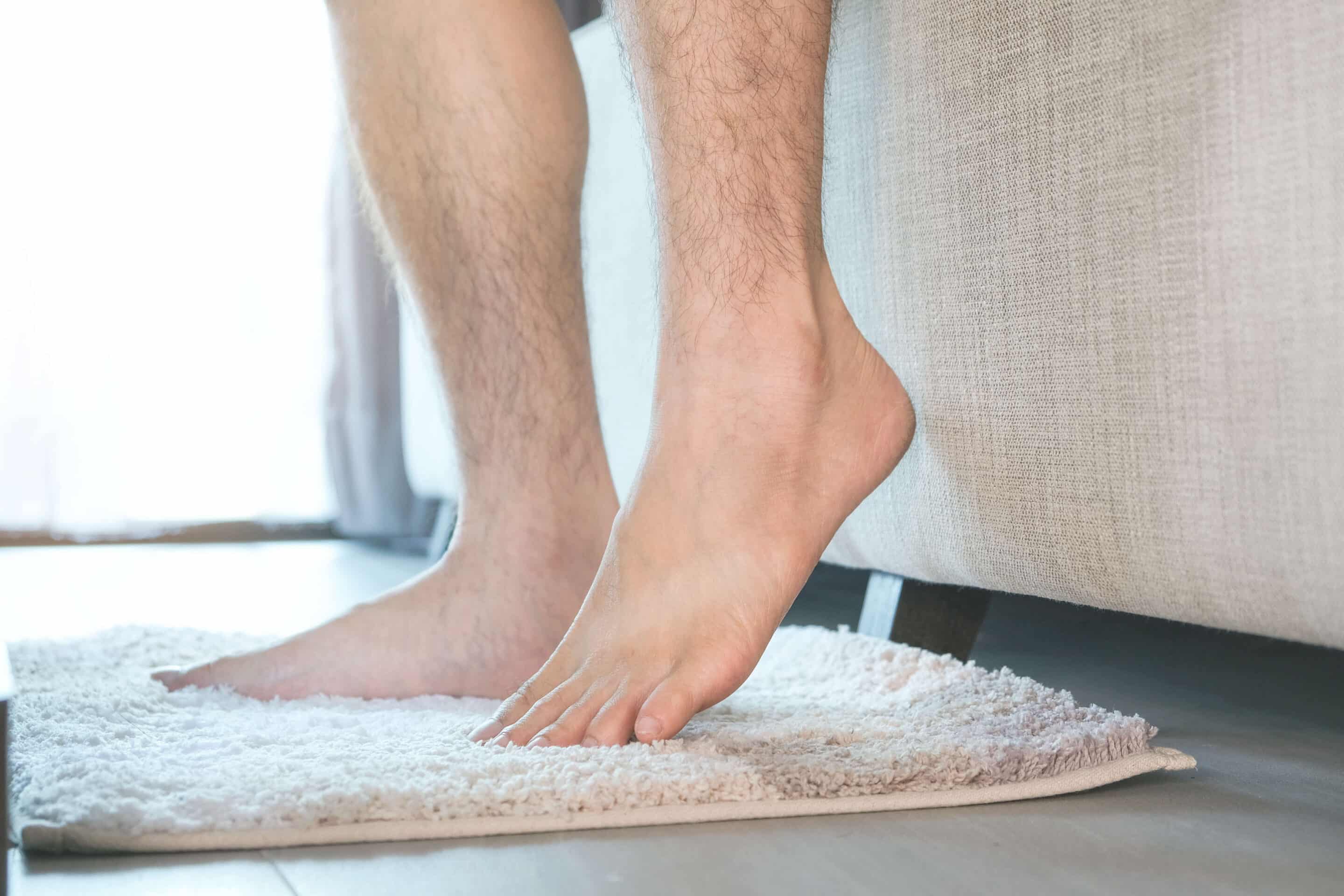 The man's legs are lifted with heels and laid on the carpet. he sits on the sofa in the living room of the house